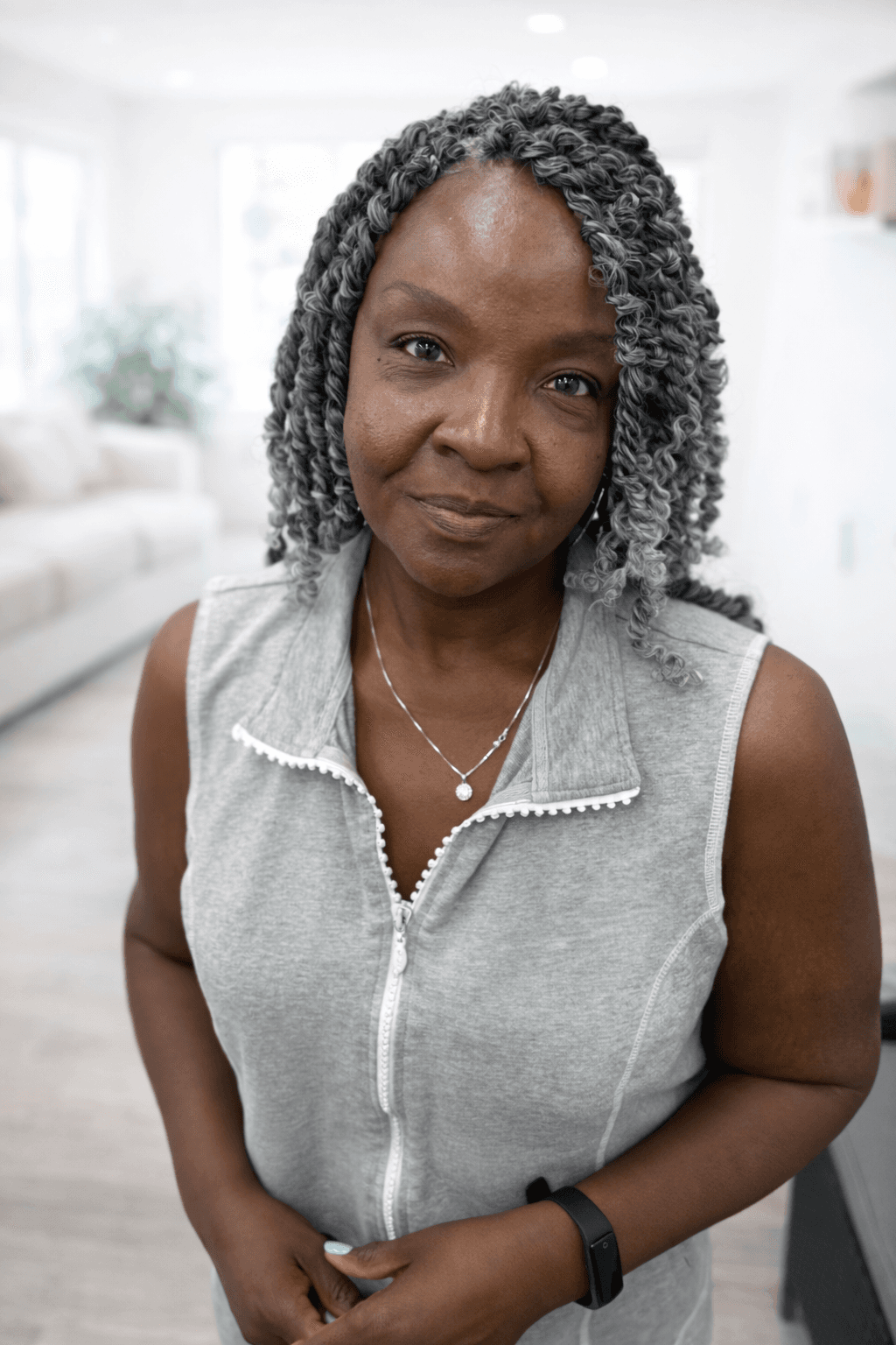 Smiling older Black woman with grey curly hair wearing a grey sleeveless zip-up top.